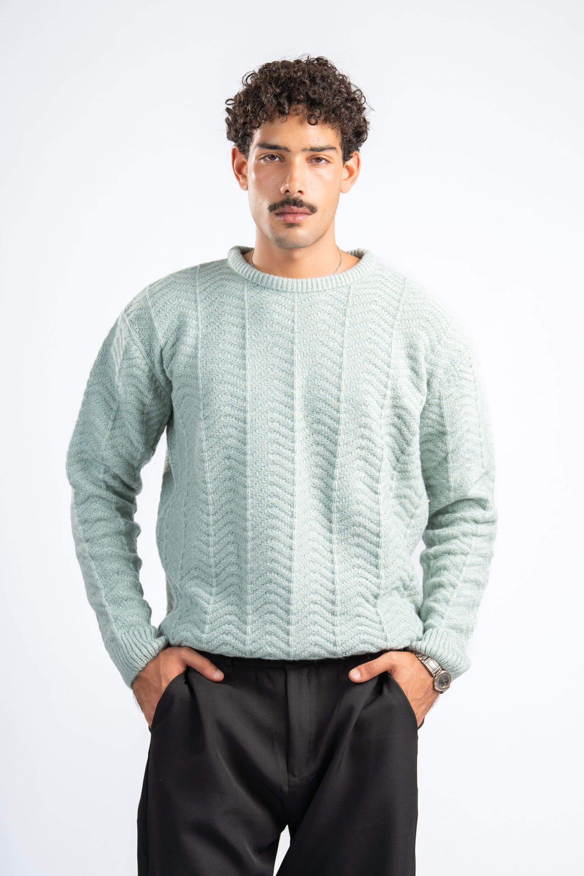 Man wearing a light green sweater and black pants on a white background