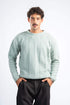 Man wearing a light green sweater and black pants on a white background