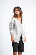 Woman wearing a light gray cardigan over a black top and shorts on a white background