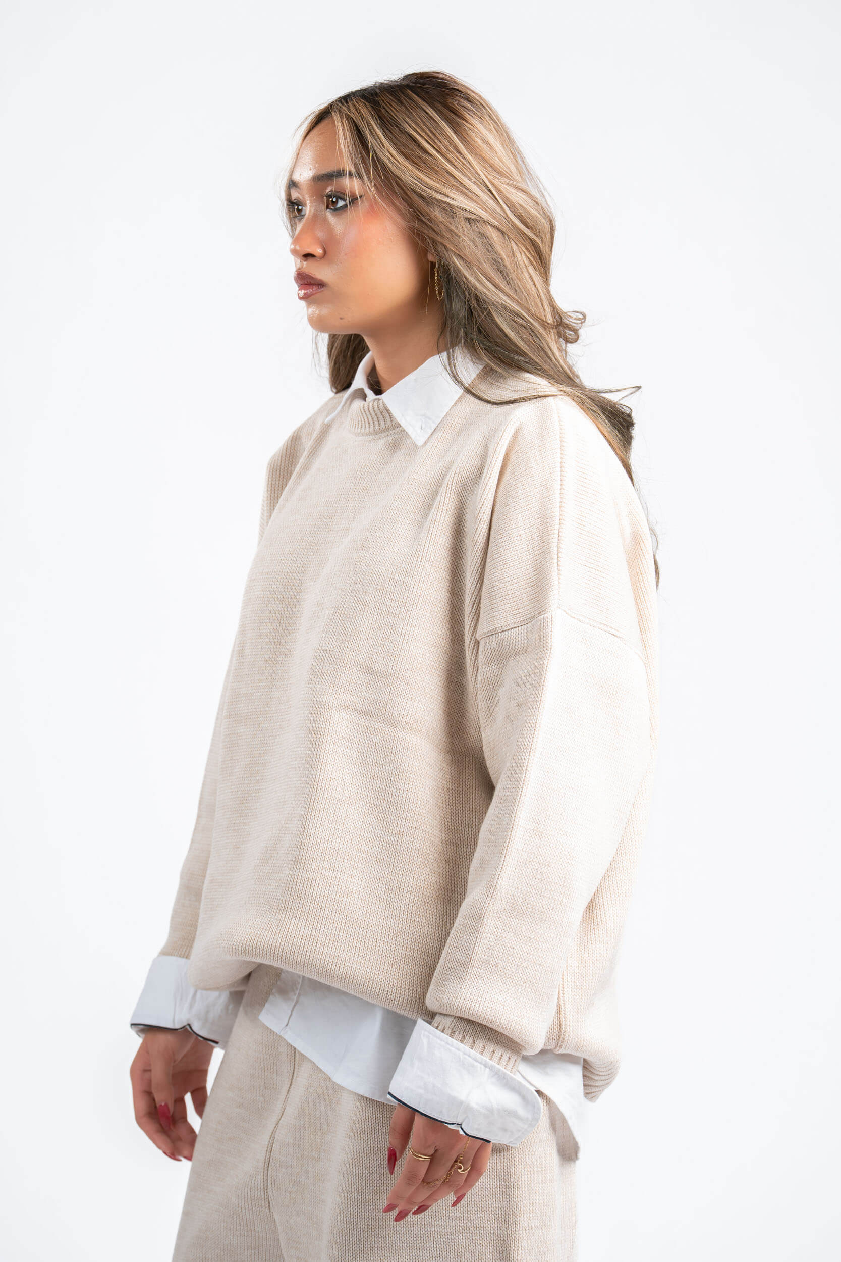 Woman wearing a beige sweater over a white shirt on a white background