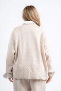 Person wearing a beige cardigan and pants on a white background