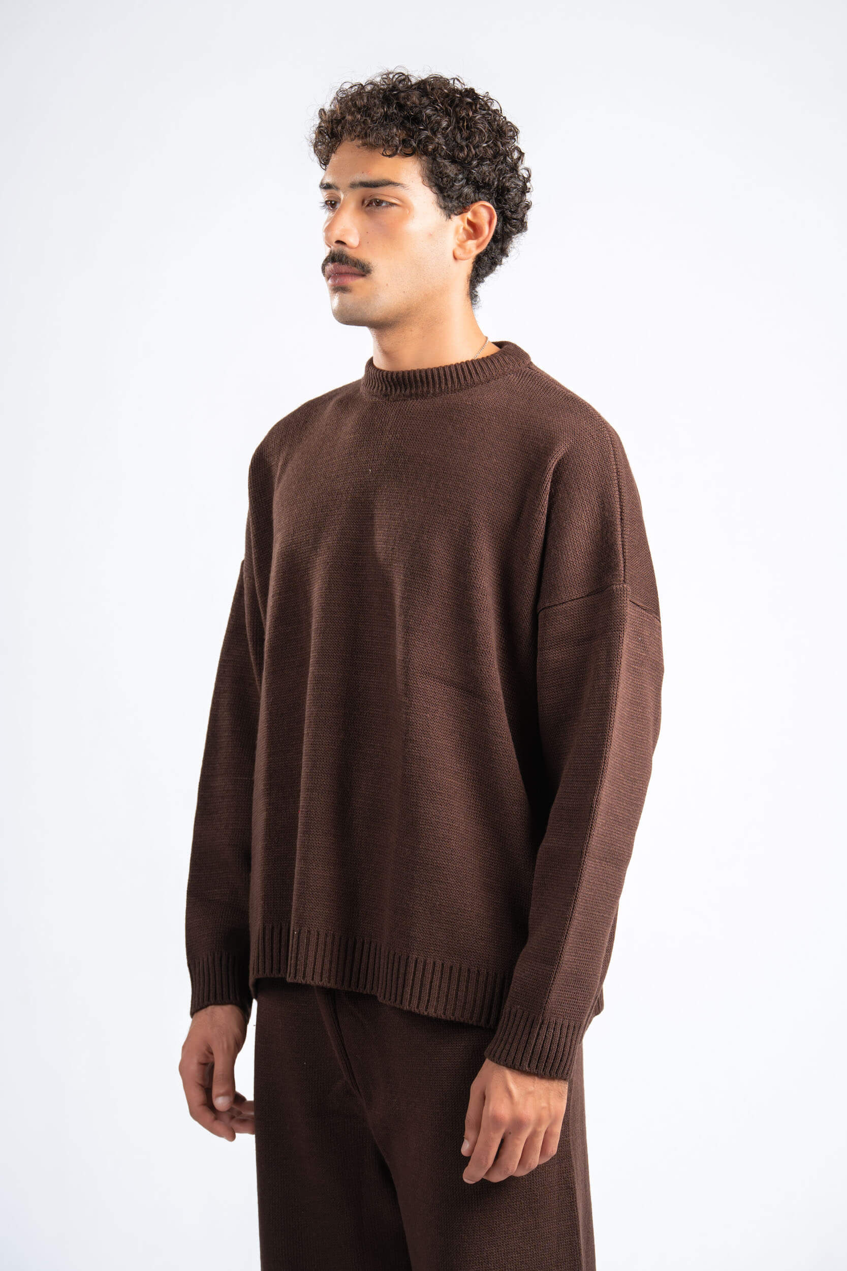 Man wearing a brown sweater and pants on a white background