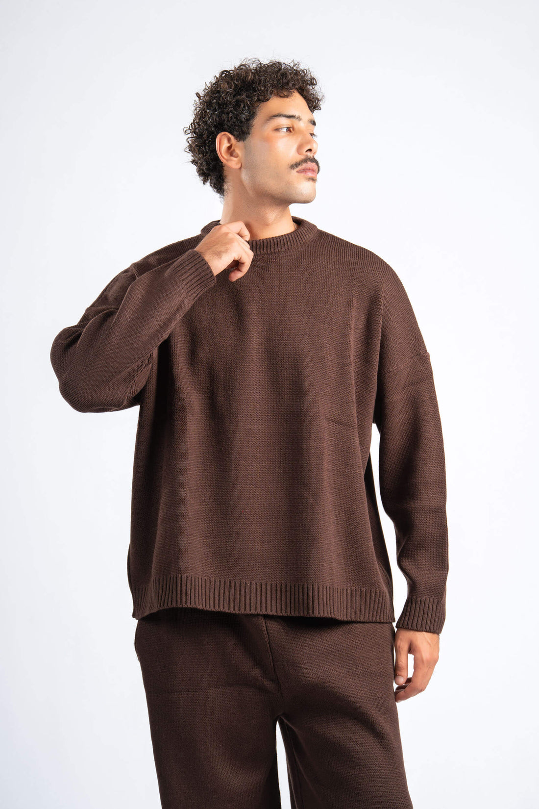 Two people wearing matching brown sweaters and pants on a plain background
