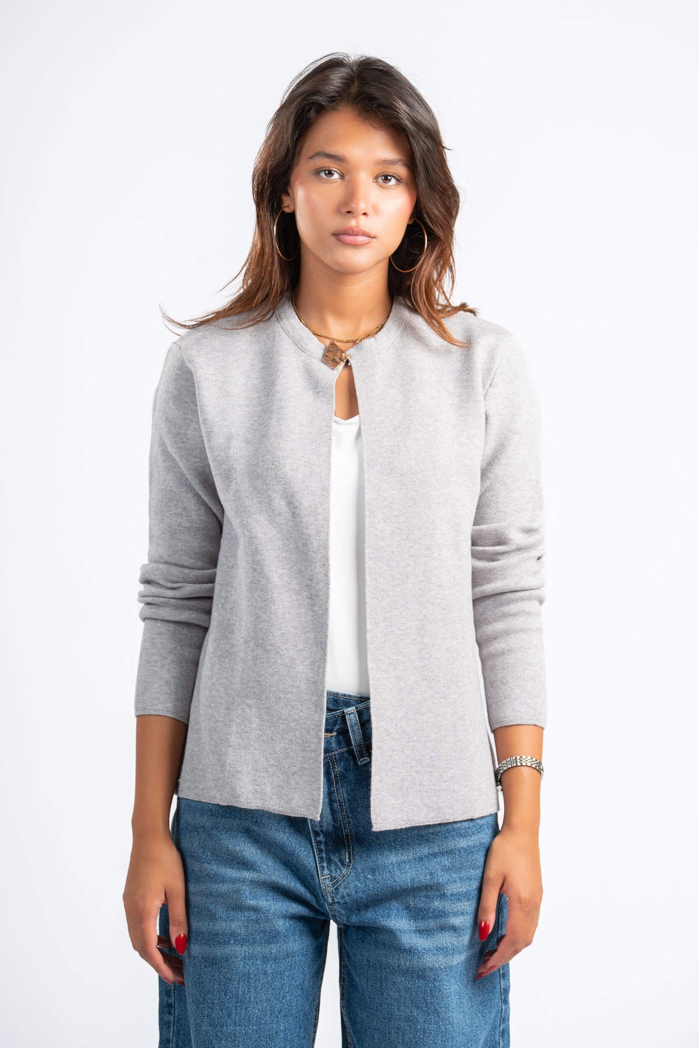 Woman wearing a gray cardigan over a white shirt and blue jeans on a white background