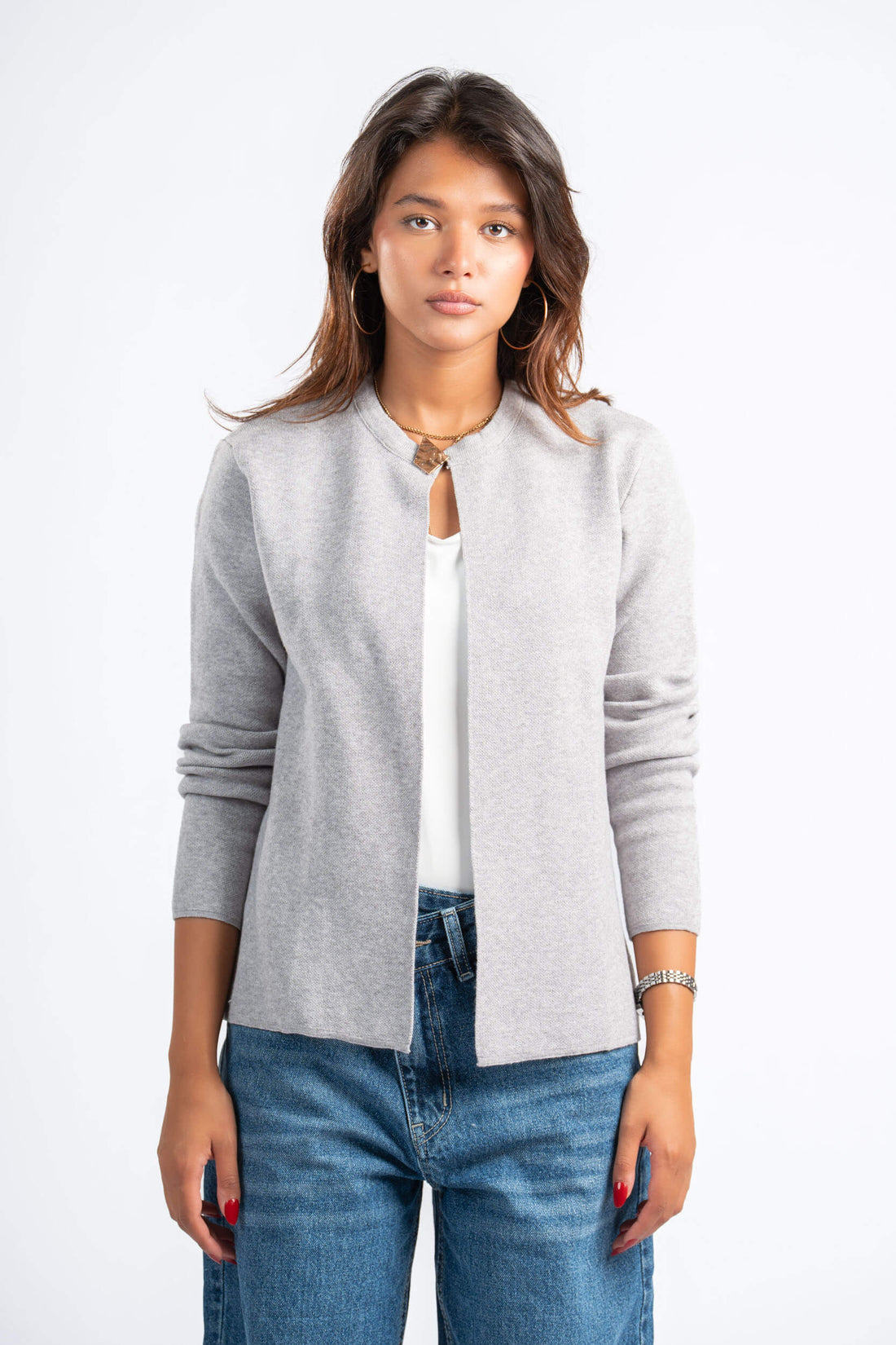 Woman wearing a gray cardigan over a white shirt and blue jeans on a white background