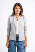 Woman wearing a gray cardigan over a white shirt and blue jeans on a white background
