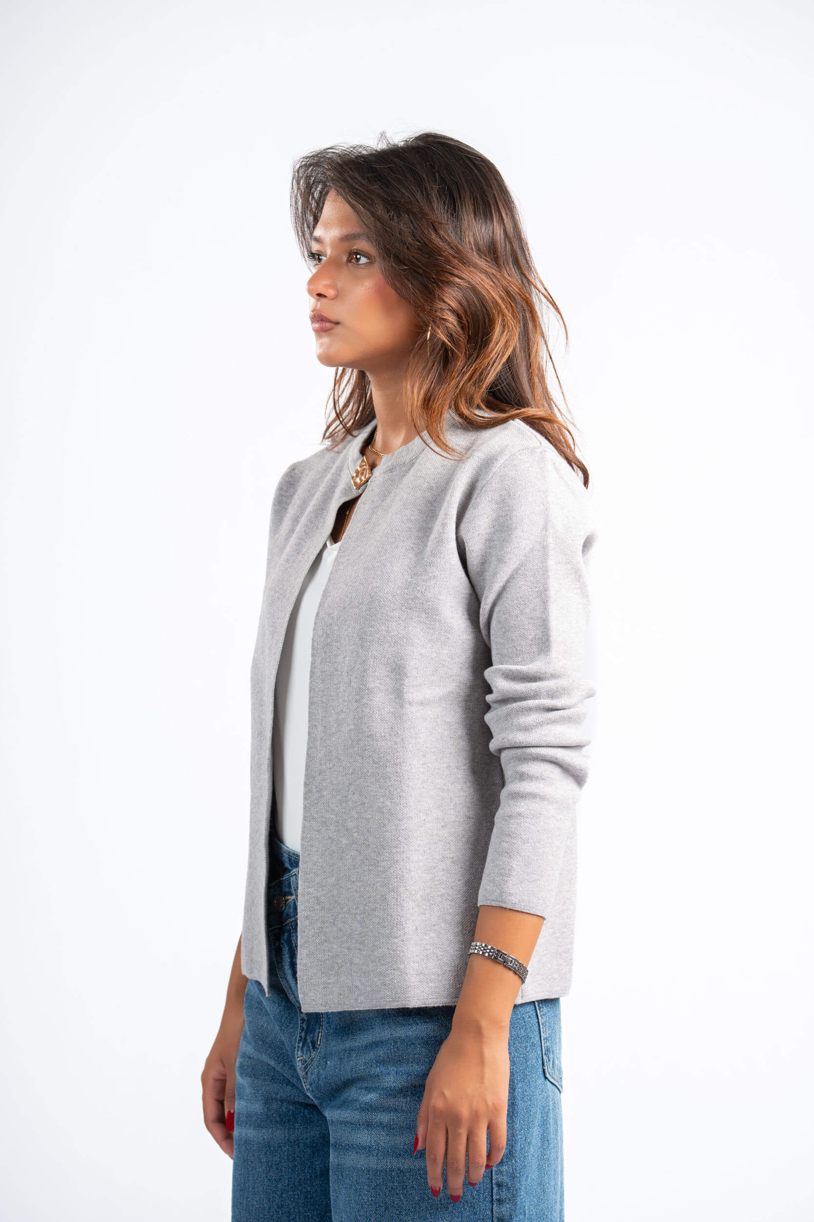 Woman wearing a gray cardigan over a white shirt with blue jeans on a white background