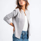 Woman wearing a light gray cardigan over a white top with blue jeans on a white background