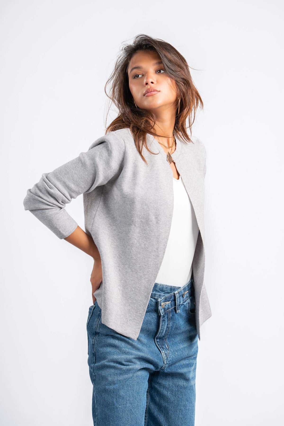Woman wearing a light gray cardigan over a white top with blue jeans on a white background