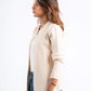 Woman wearing a beige cardigan over a light blue top and blue jeans on a white background