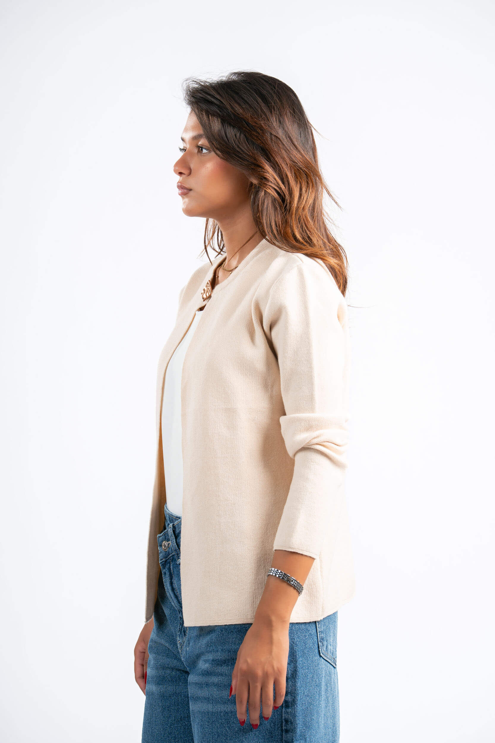 Woman wearing a beige cardigan over a light blue top and blue jeans on a white background