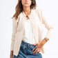 Woman wearing a beige blazer, white top, and blue jeans on a white background