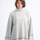 Woman wearing a light gray ribbed sweater with red trim on a white background