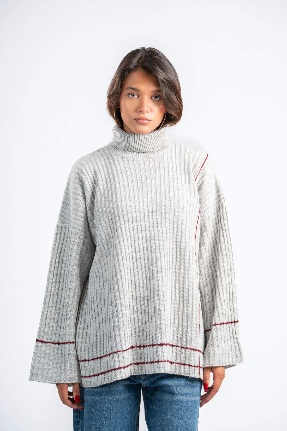 Woman wearing a light gray ribbed sweater with red trim on a white background