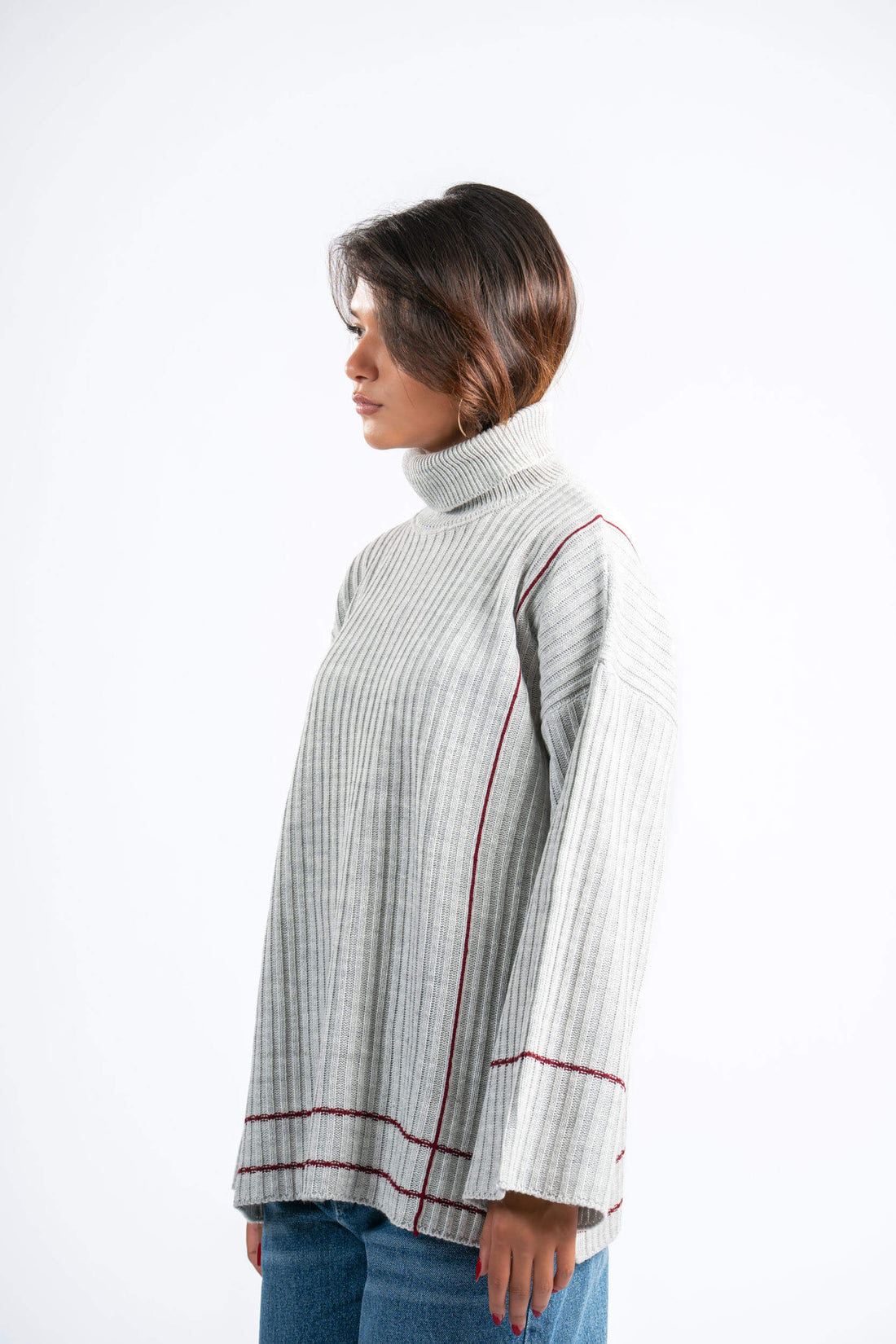 Woman wearing a light gray ribbed sweater with red trim on a white background