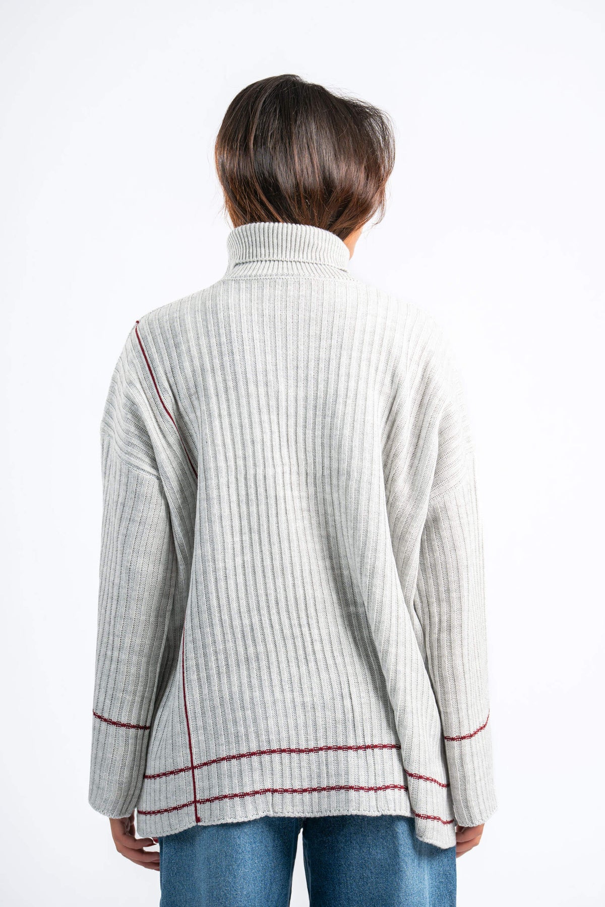 Person wearing a light gray ribbed sweater with red accents on a white background