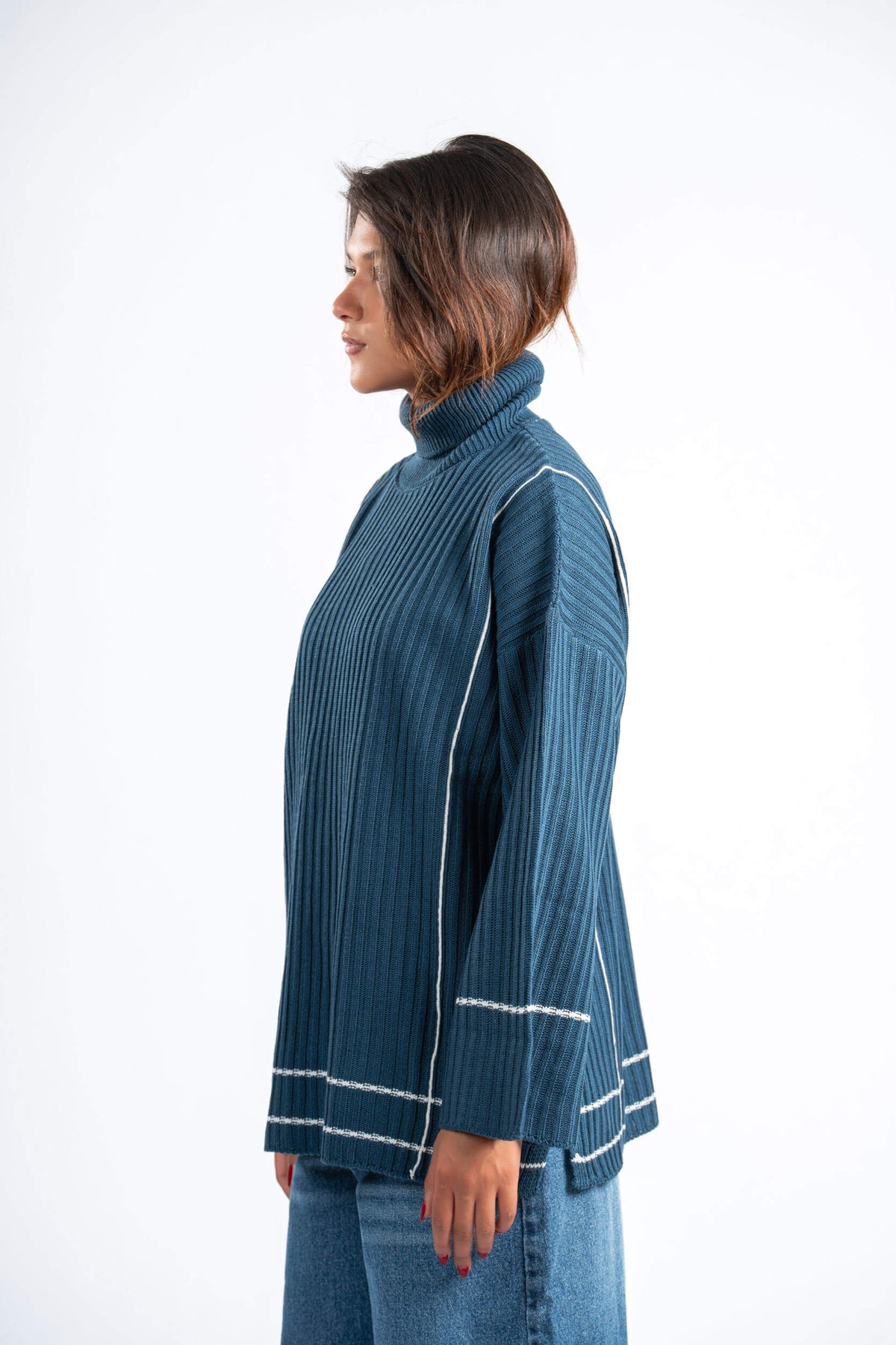 Woman wearing a blue ribbed sweater with white piping on a white background