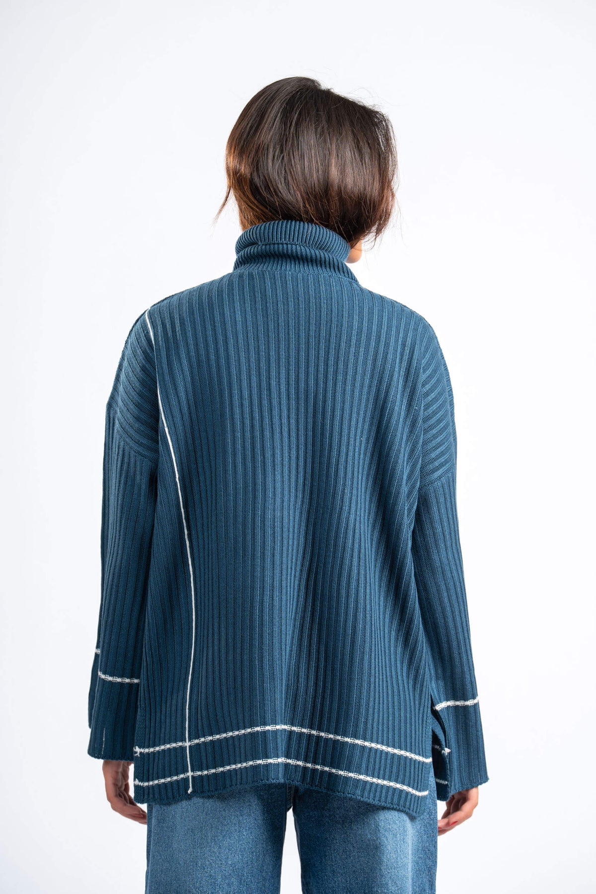 Person wearing a blue ribbed sweater with white trim on a white background