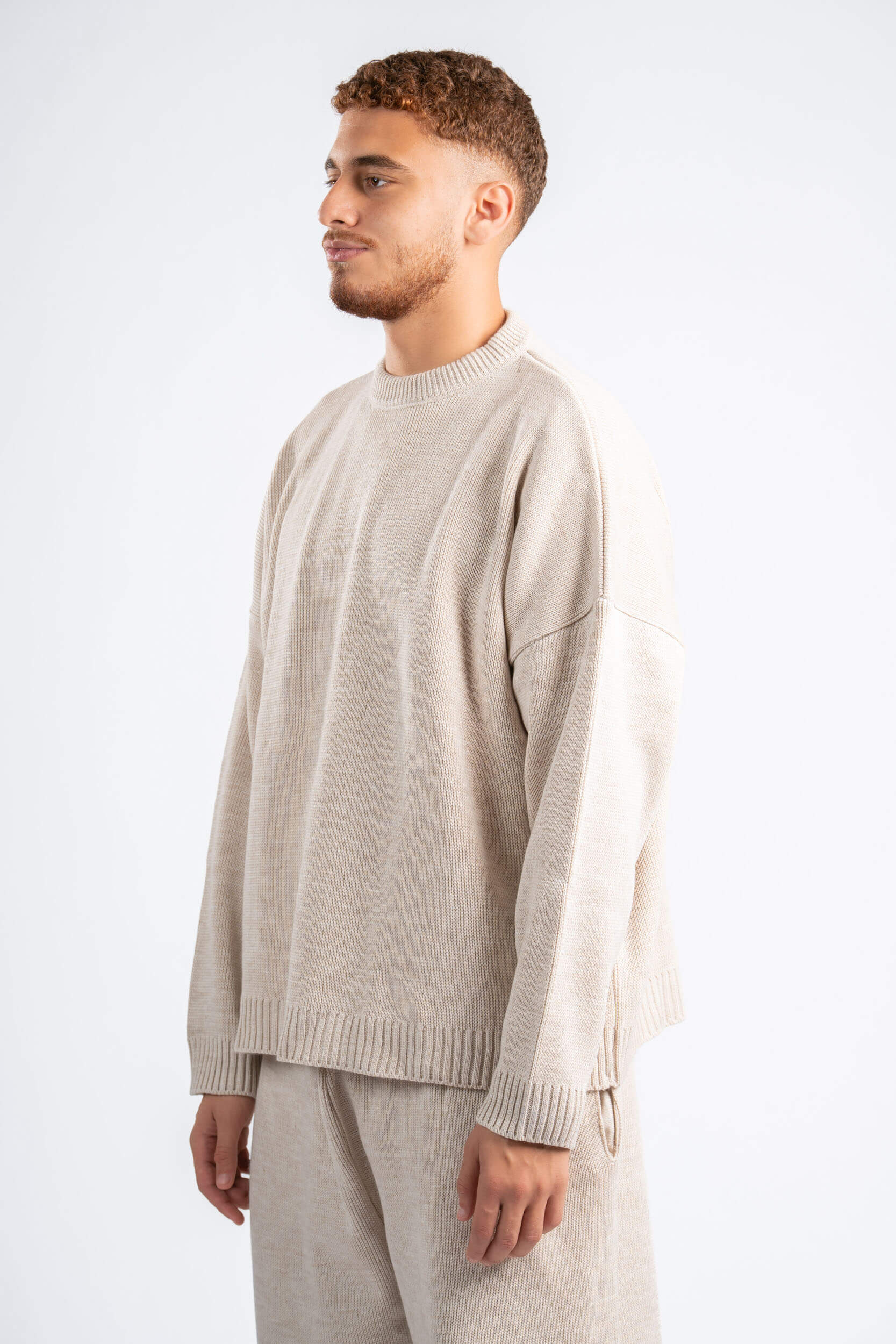 Man wearing a beige sweater and pants on a white background