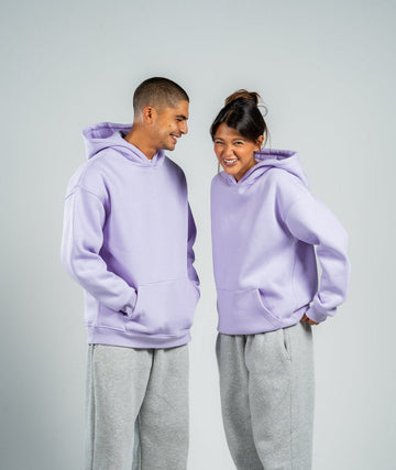 Two people wearing matching lavender hoodies and gray pants on a white background