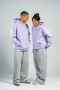 Two people wearing matching lavender hoodies and gray pants on a white background