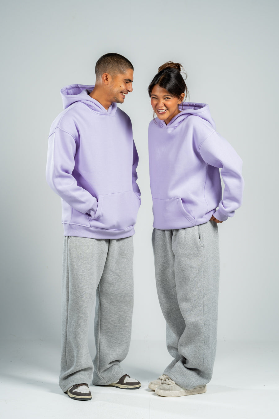 Two people wearing matching lavender hoodies and gray pants on a white background