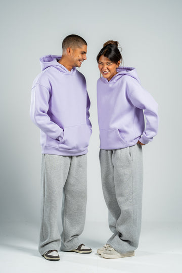 Two people wearing matching lavender hoodies and gray pants on a white background