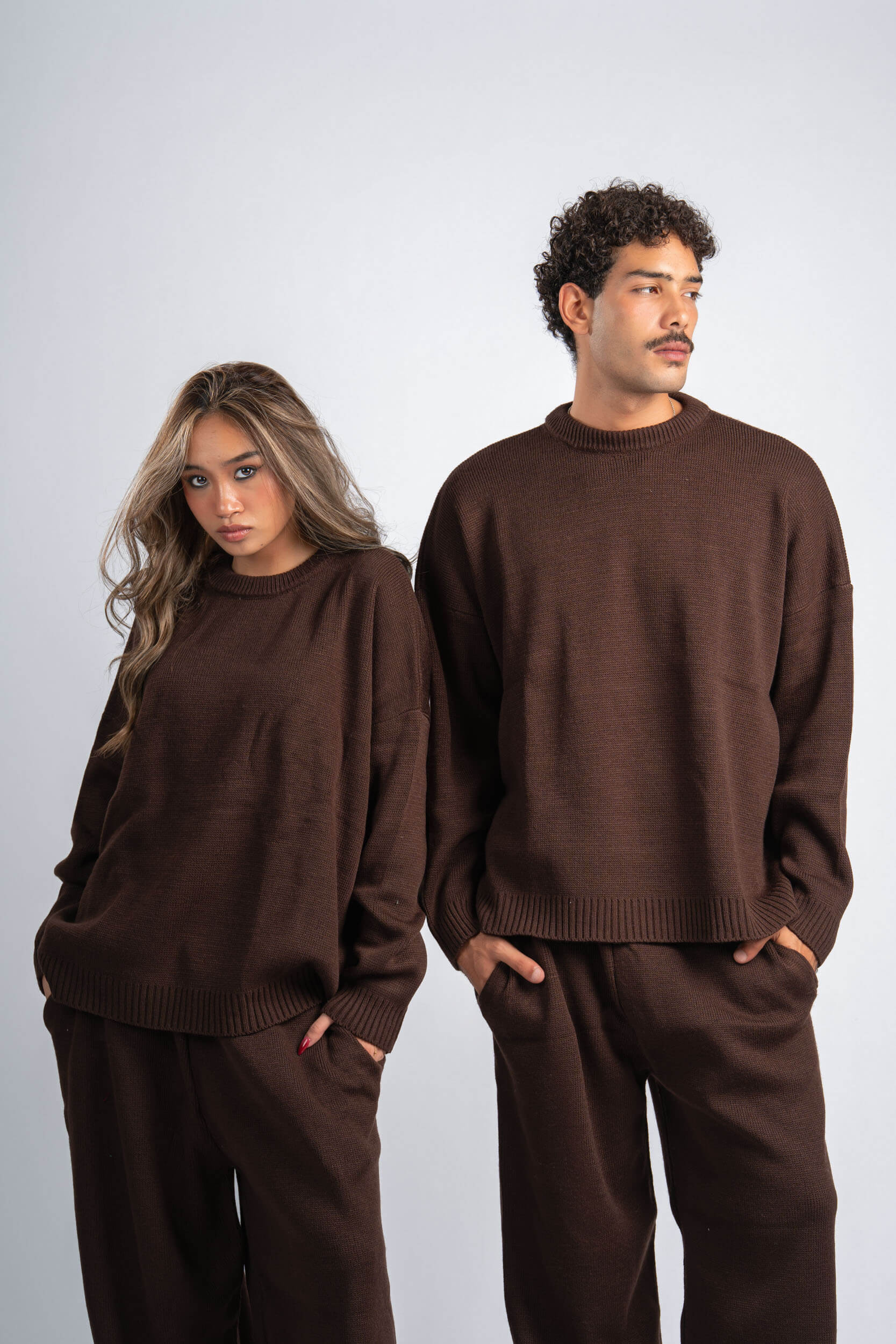 Two people wearing matching brown sweaters and pants on a plain background