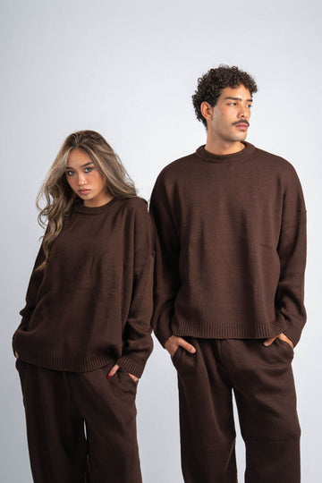 Two people wearing matching brown sweaters and pants on a plain background