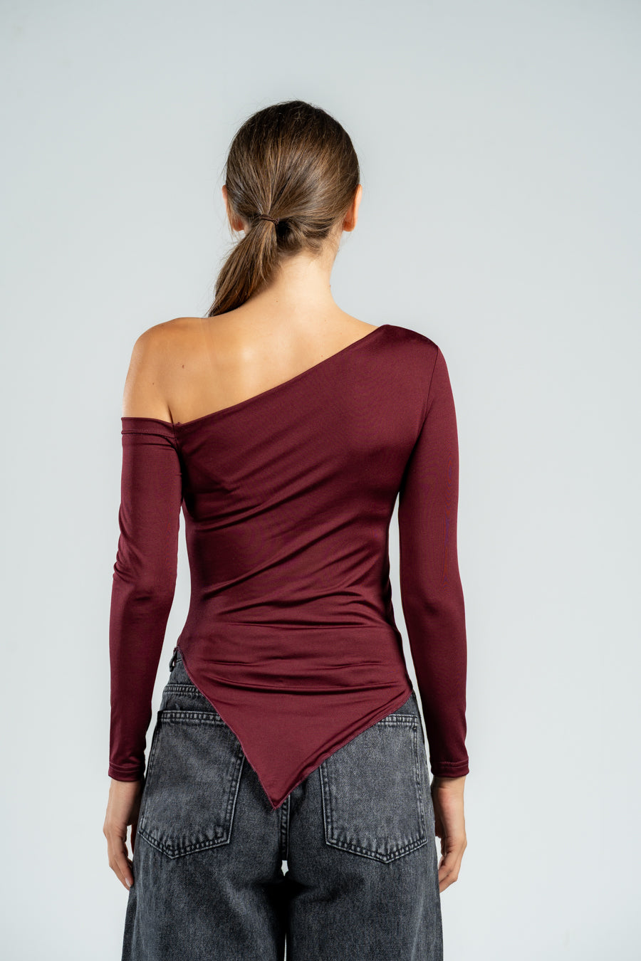 Person wearing a burgundy one-shoulder top and gray pants on a light gray background