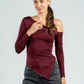 Woman wearing a burgundy off-shoulder top and gray jeans on a light gray background