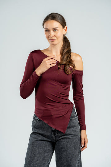 Woman wearing a burgundy off-shoulder top and gray jeans on a light gray background