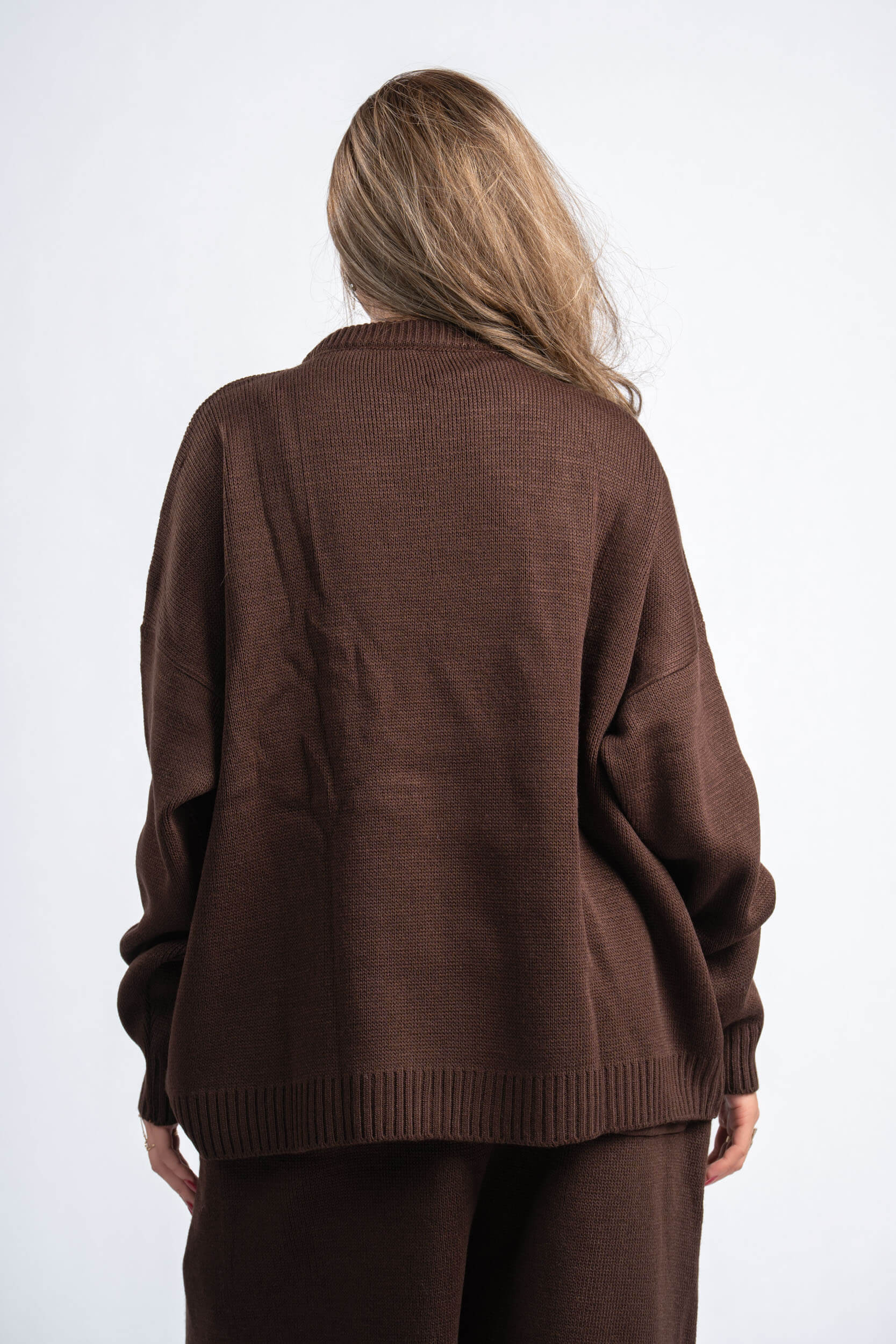 Person wearing a brown sweater and pants on a white background