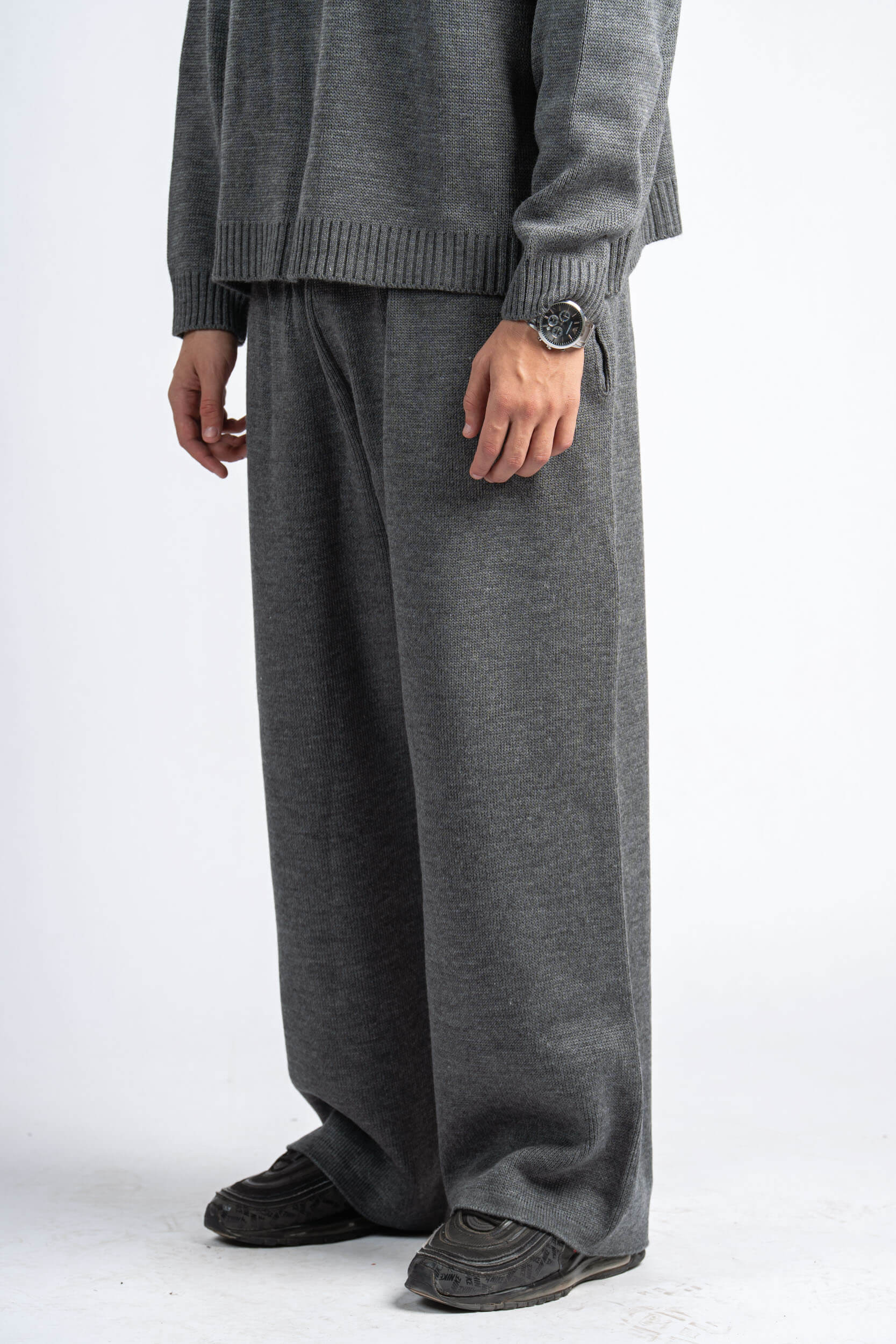 Person wearing a gray sweater and pants on a white background