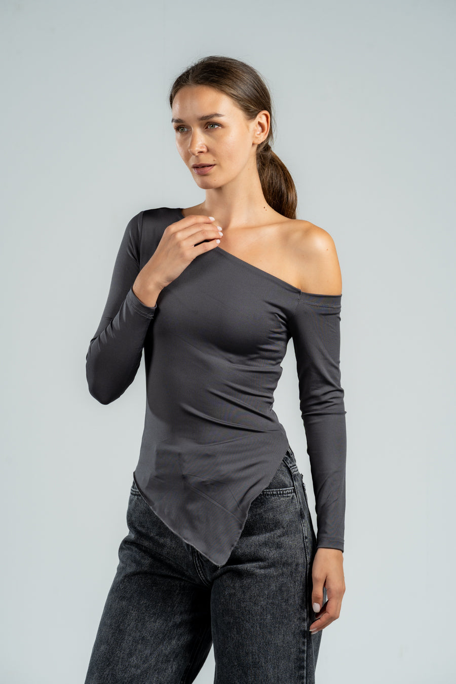 Woman wearing a gray off-shoulder top and jeans on a light gray background