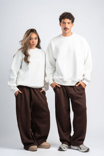 Two people wearing white sweaters and brown pants against a white background