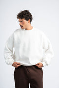 Person wearing a white sweater and brown pants on a light gray background