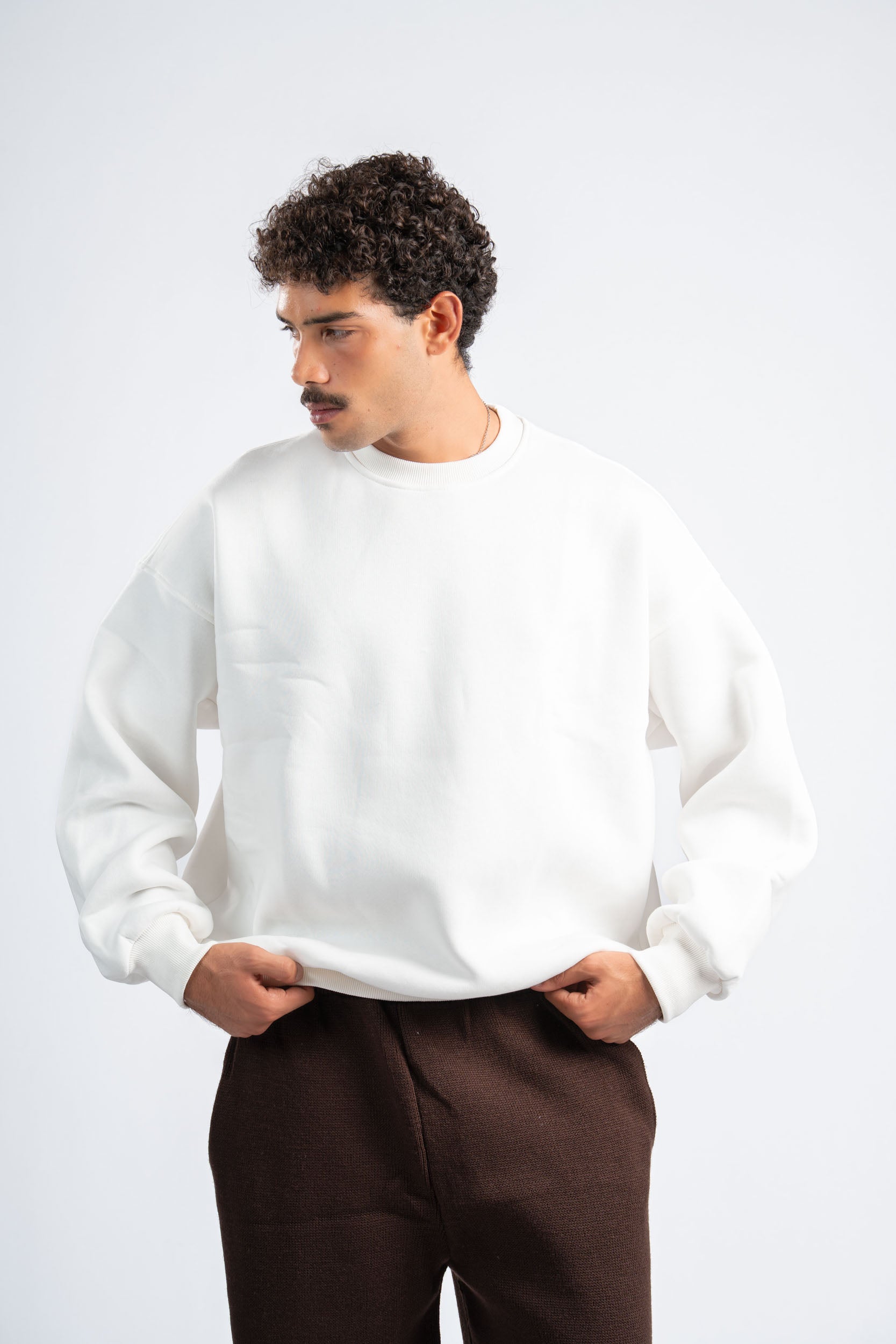 Person wearing a white sweater and brown pants on a light gray background