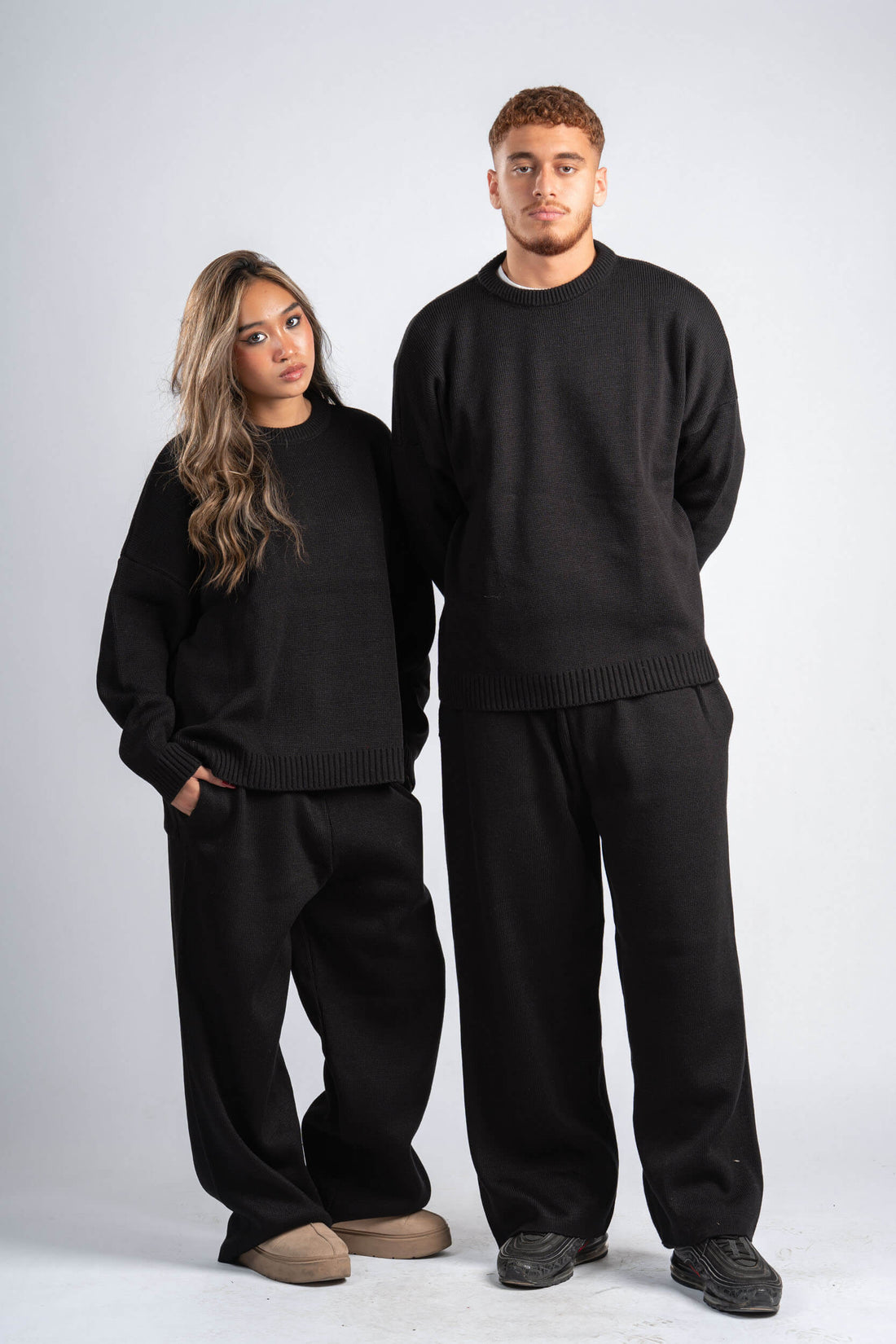 Two people wearing matching black sweaters and pants on a white background