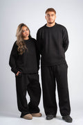 Two people wearing matching black sweaters and pants on a white background