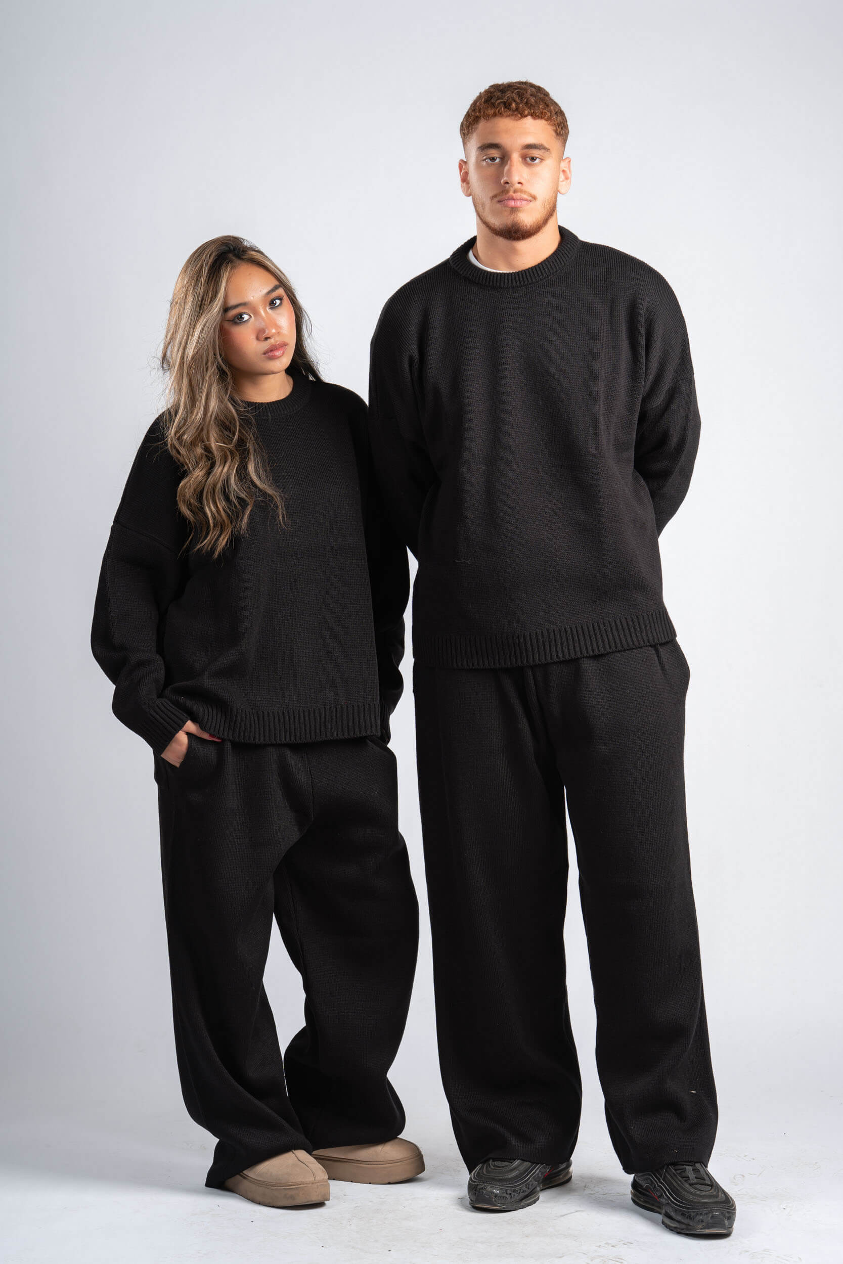 Two people wearing matching black sweaters and pants on a white background