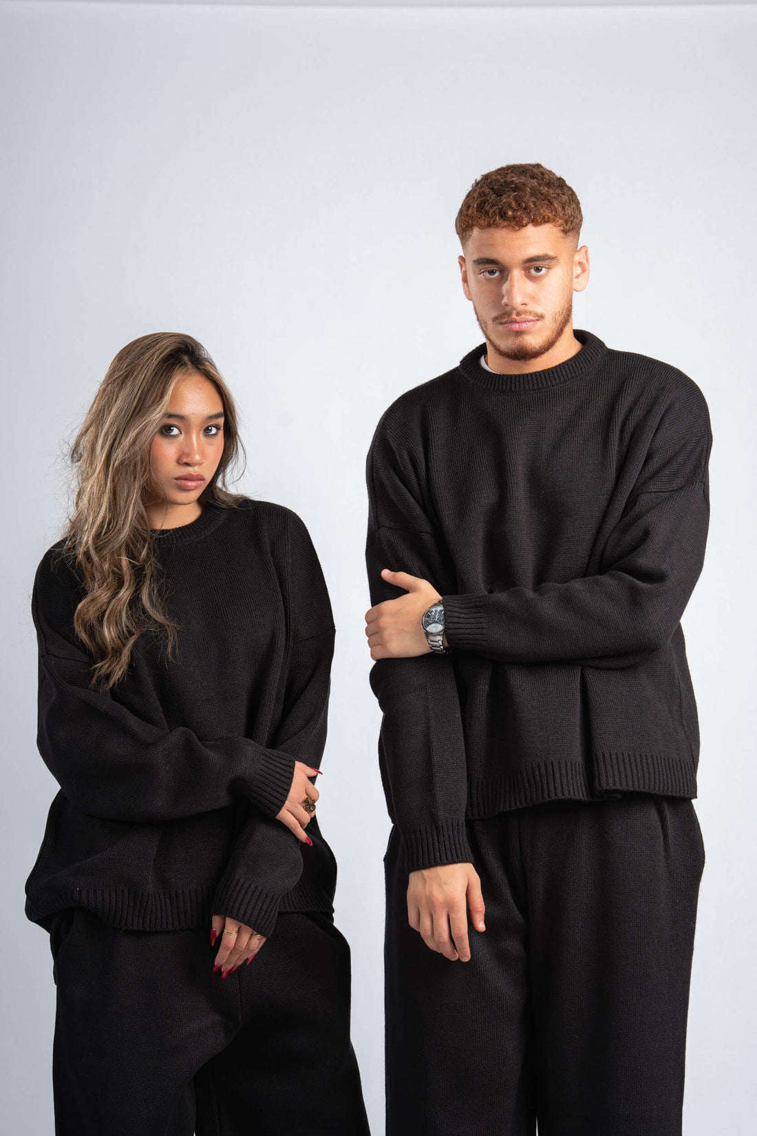 Two people wearing matching black outfits against a plain background