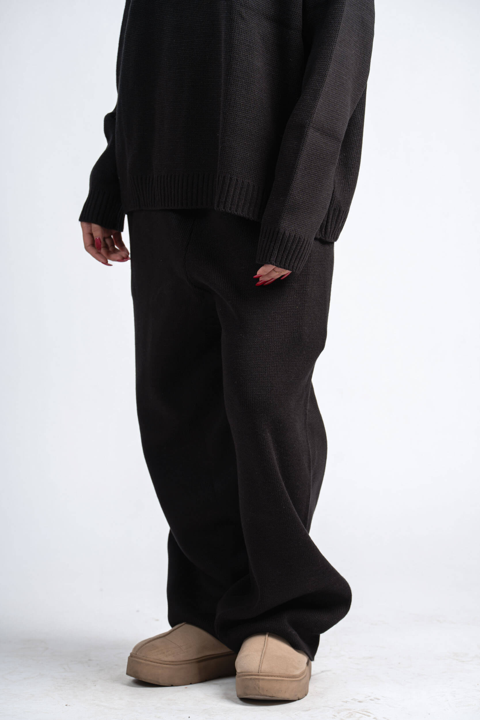 Person wearing a dark sweater and pants with beige shoes on a white background