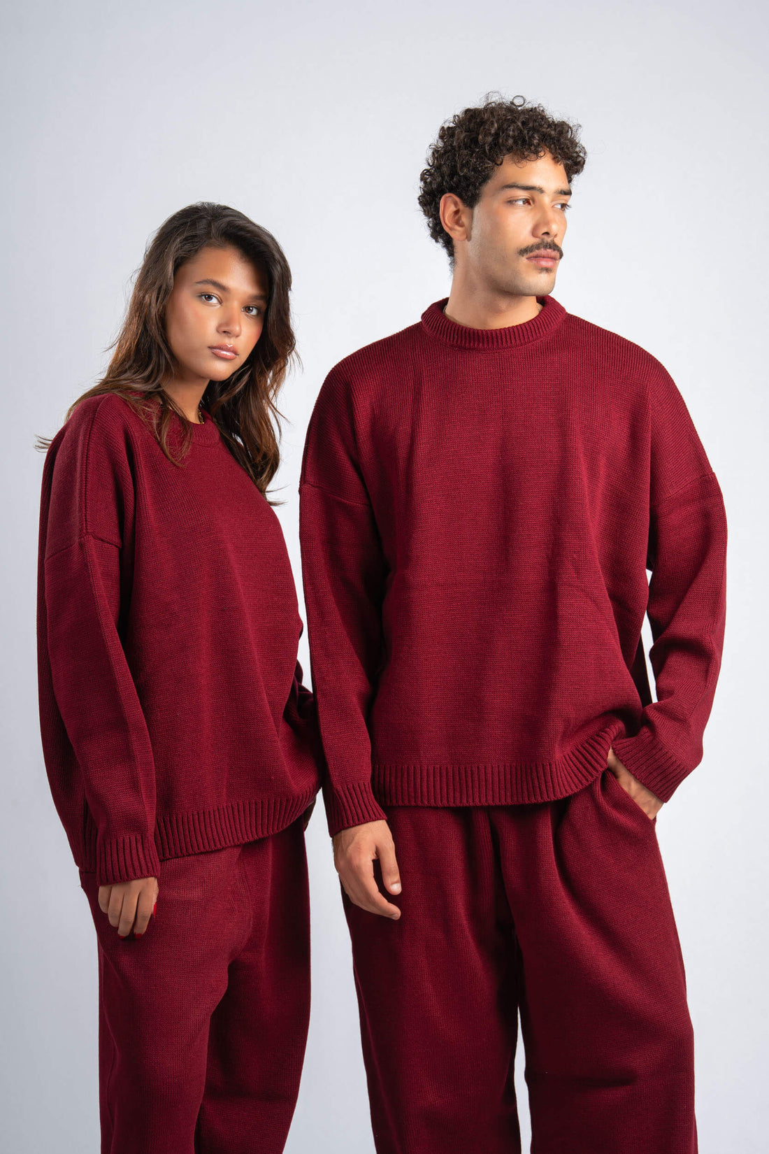 Two people wearing matching red sweaters and pants on a white background