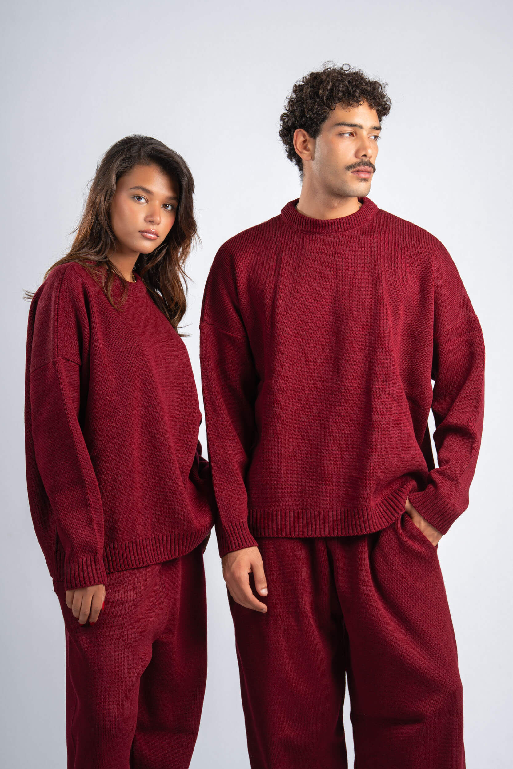 Two people wearing matching red sweaters and pants on a white background