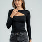 Woman wearing a black long-sleeve top with cut-out design and high-waisted dark jeans on a light gray background