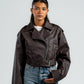 Person wearing a brown leather jacket and blue jeans against a plain background