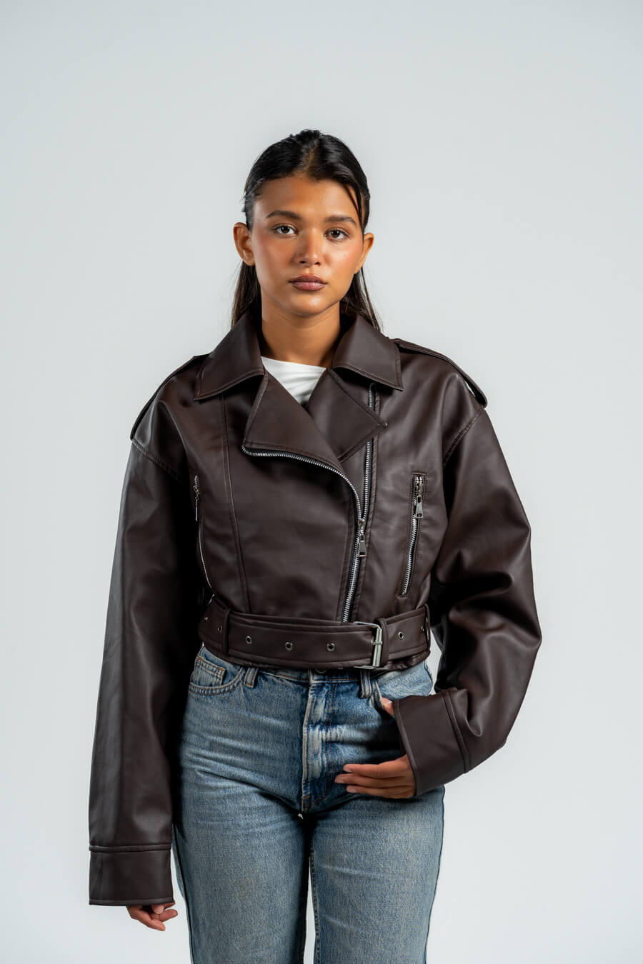 Person wearing a brown leather jacket and blue jeans against a plain background