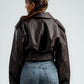 Person wearing a brown leather jacket and blue jeans on a plain background