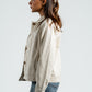 Woman wearing a beige jacket and blue jeans against a white background